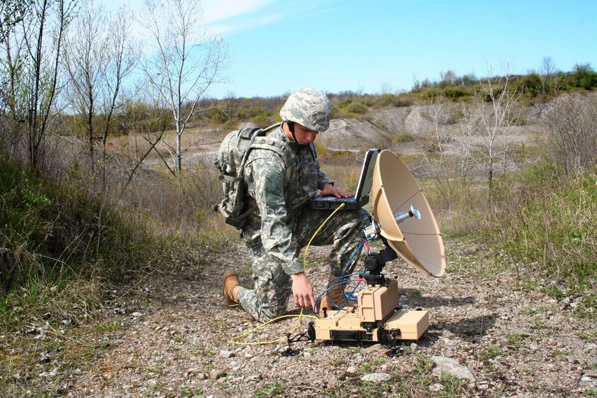 Soldier with a laptop working on a satelitte antenna.